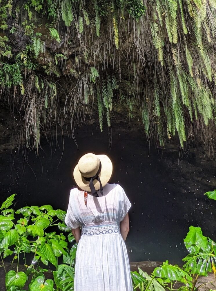 Allison wearing a sunhat and a white cover up while looking up at cave geology and tropical flora