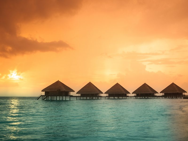 Orange sky with five overwater bungalows in Tahiti on the turquoise blue water at sunset