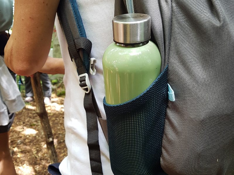 Green reusable water bottle in a sleeve of a backpack