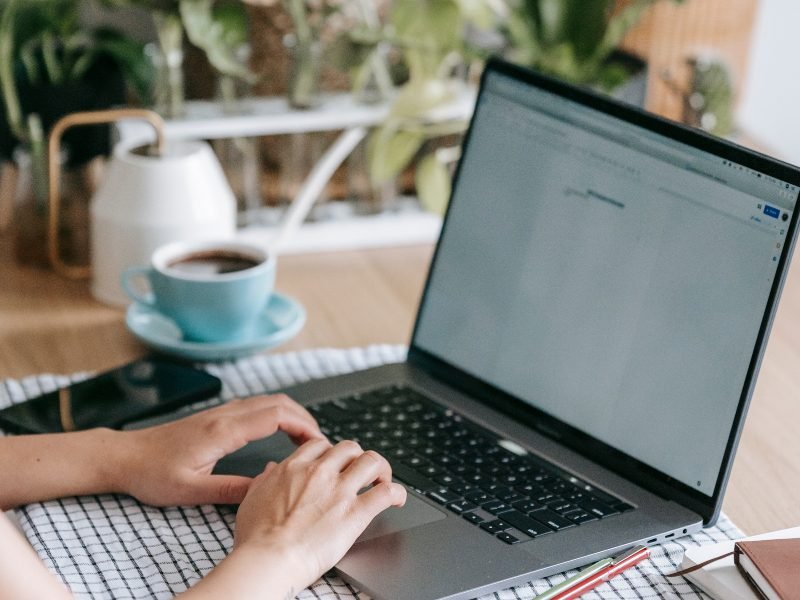 Hands on a laptop keyboard with a cup of coffee behind it