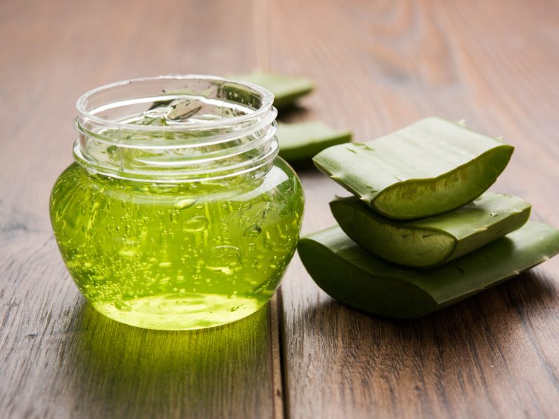 Aloe vera gel in green color in clear container with cut up aloe vera plant next to it