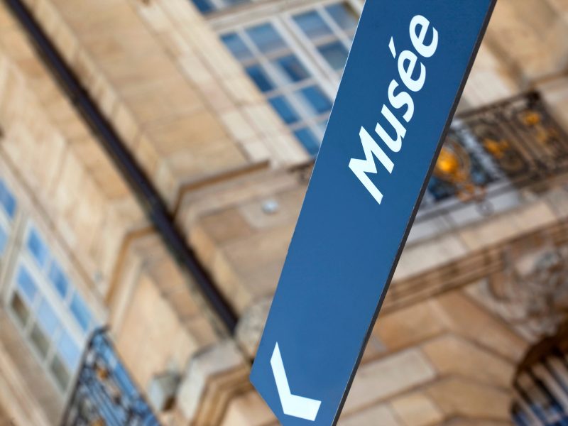 blue street sign pointing to the left that says 'musee