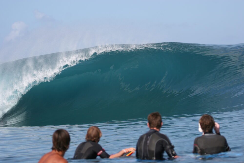 People watching the waves at Teahupoo, four surfers in the water looking at a barrel wave