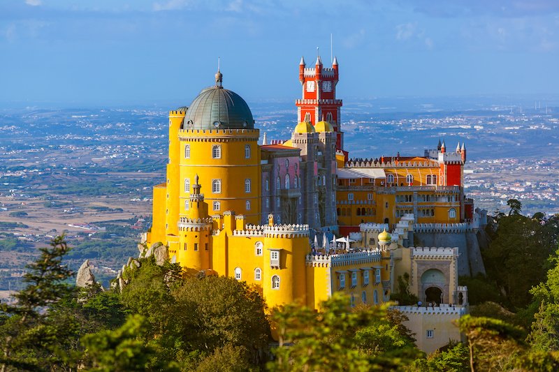 Pena Palace in Sintra - Portugal - red and yellow castle with the rolling hills of sintra and the surrounding landscape in the background