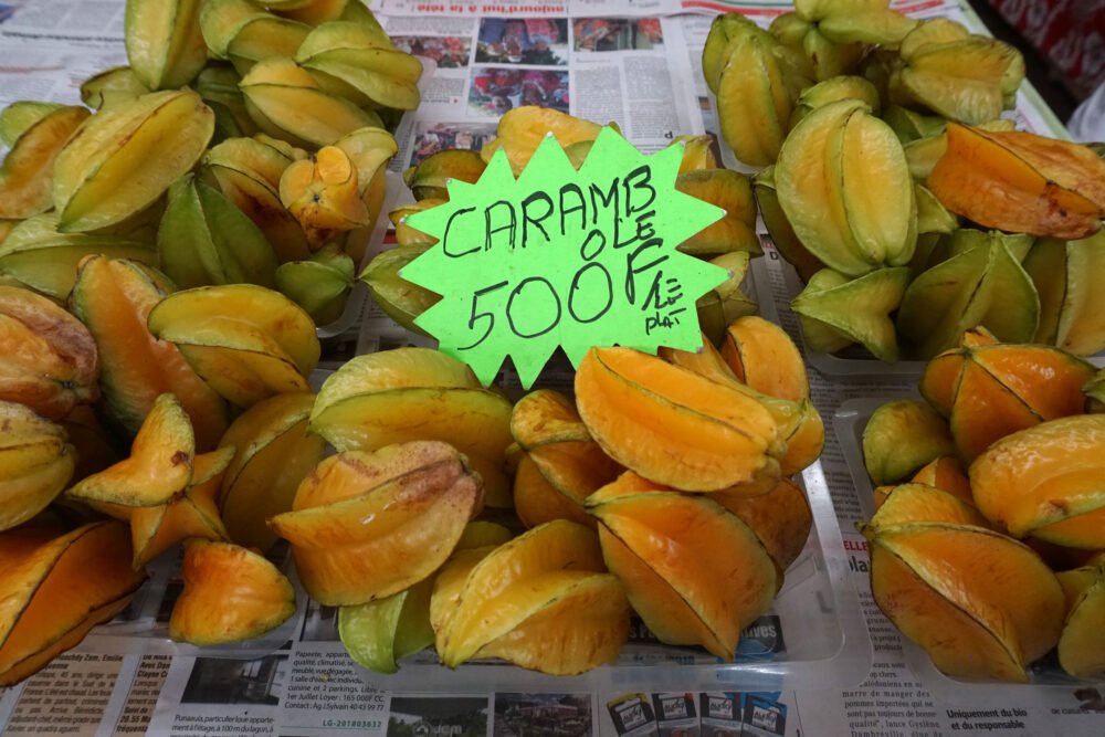 A sign that reads "carambole" which is French for star fruit, with orange and yellow star-shaped fruits for display on newspaper in the market.