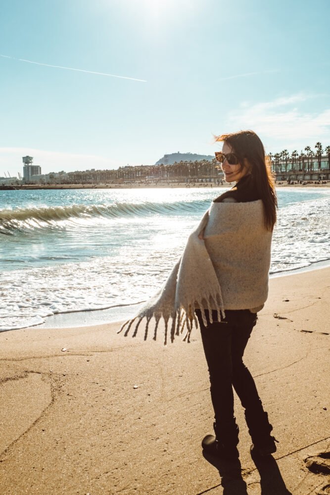 Woman in Barcelona walking on the beach with a shawl to warm her up