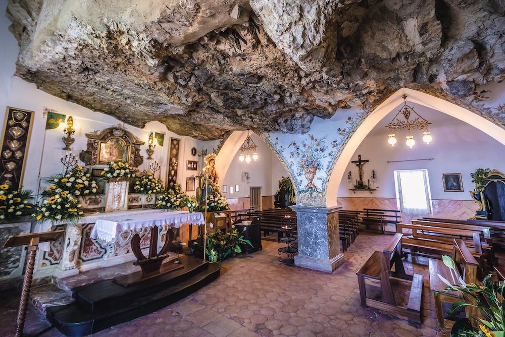 Chapel built into the rock, with a stone roof, archways holding up the roof, and pews