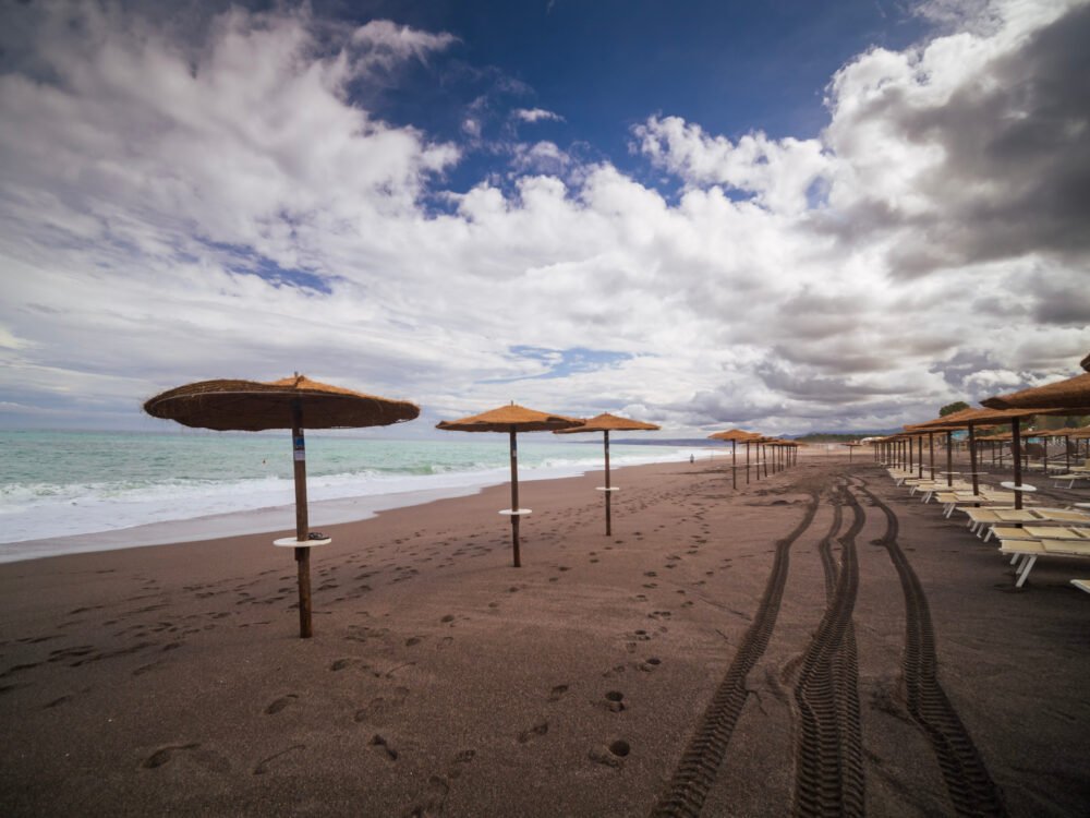 Umbrellas with thatch-style roofing on a quiet beach near Taormina on a cloudy, overcast day