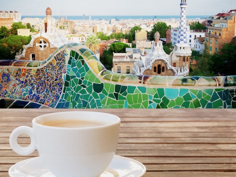 Person enjoying a cup of coffee while sitting outside at the colorful Park Guell in Barcelona, a famous landmark of the city
