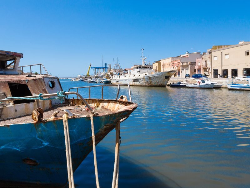 Boat with water reflecting onto it, other boats in the harbor of Mazara del Vallo, a historic Sicilian waterfront town.