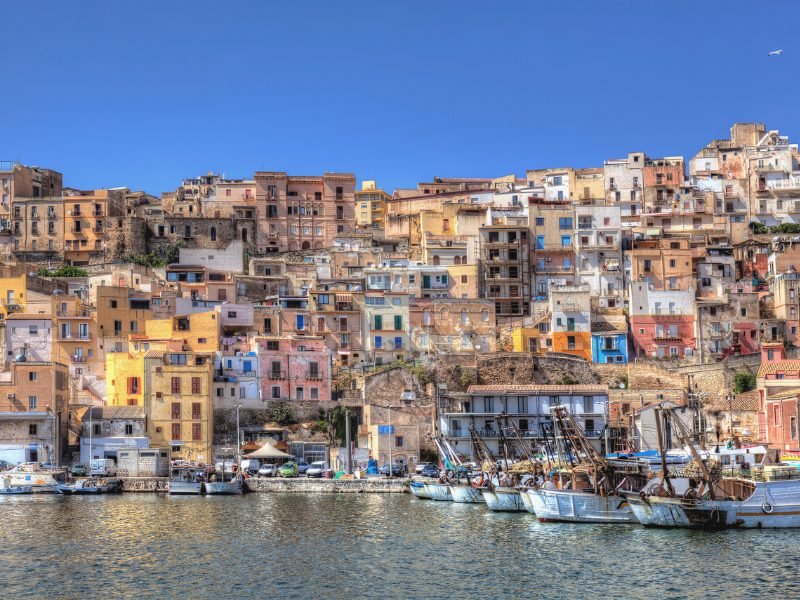 The colorful wall of buildings in all different colors as seen from the water approaching Sciacca harbor