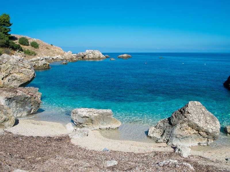 The rocky coastline of Scopello and the beach in the main town, on a clear summer day where the sea appears cerulean blue