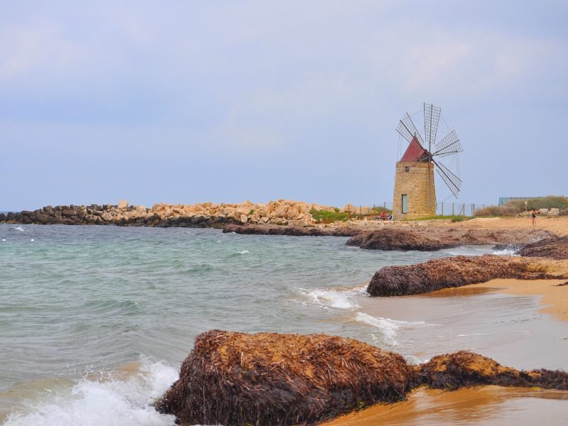 The lovely beach town of Trapani, with a windmill in its famous salt pan area, with crashing waves