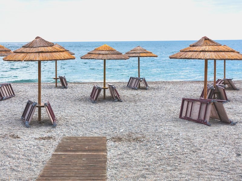 Beach umbrellas with beach chairs folded up on a lido beach club in a beach near Taormina, Sicily