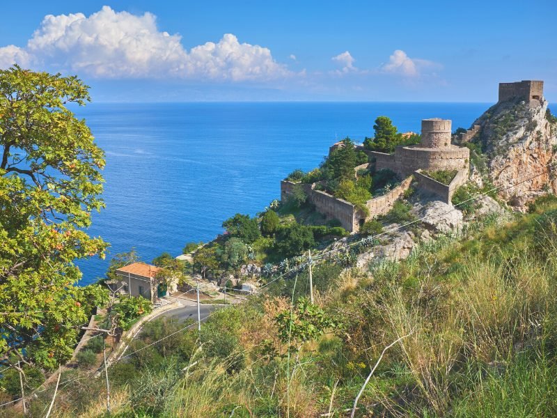 A castle overlooking the ocean in Sicily, beneath it is one of the popular beaches near Taormina