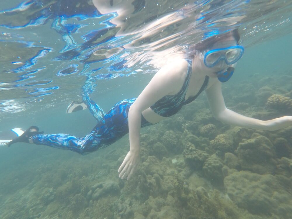 Allison snorkeling in swim leggings, a swim top, white fins, above a reef in Tahiti