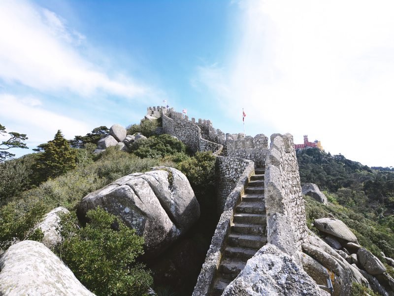The stairway to the Moorish castle in Sintra, with the red and yellow architecture of the distinctive Pena Palace visible far off in the distance