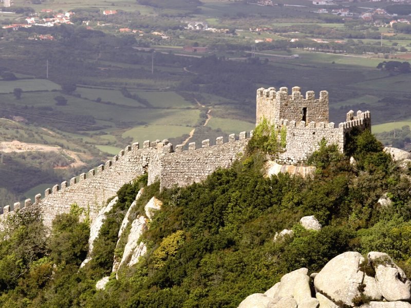 Walls of the Castelo dos Mouros (moorish castle) with view over the fields of Sintra and distant city view