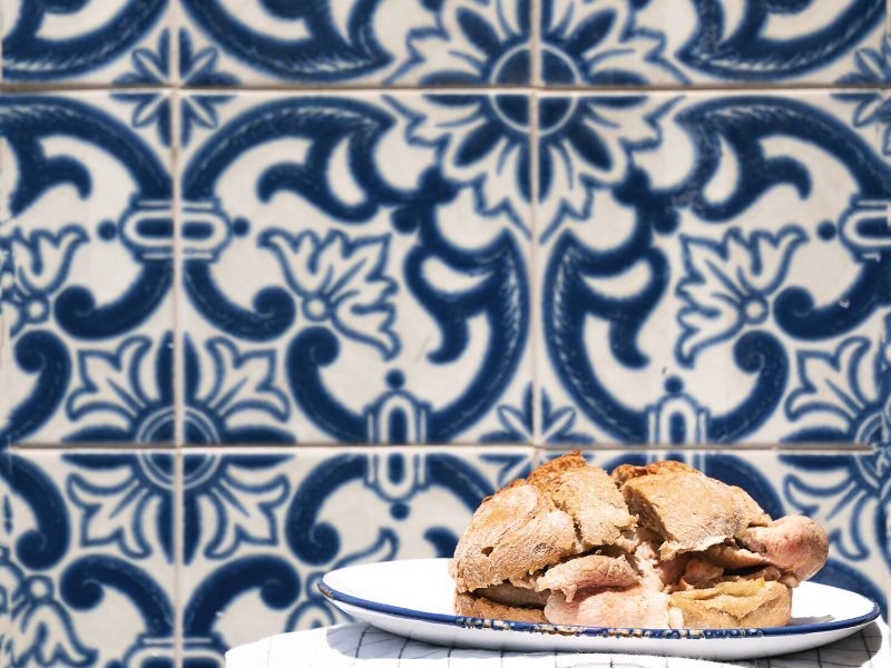 Portuguese sandwich called a bifana against a backdrop of azulejo (white and blue) tile