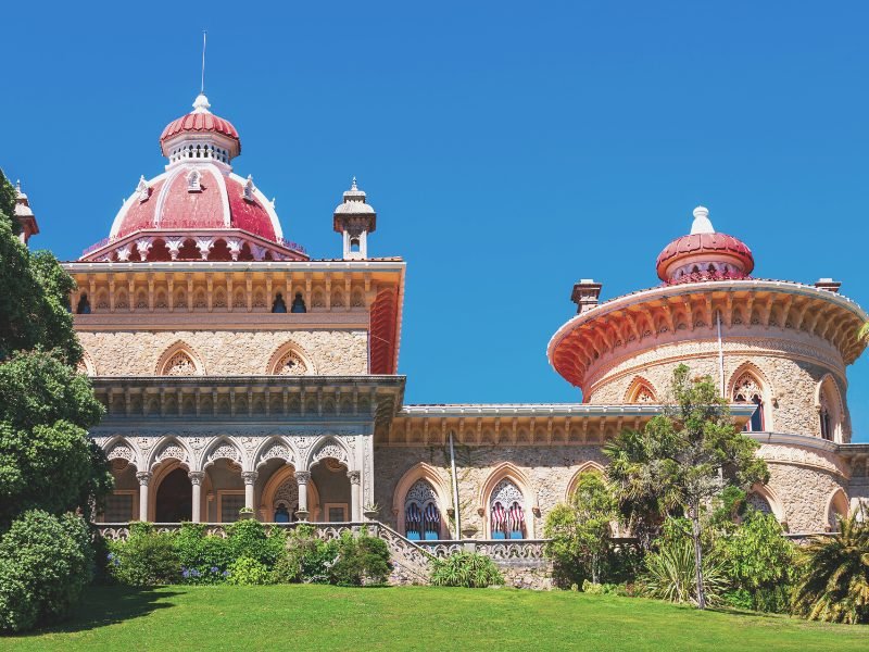 View of Monserrate Palace from the outside, archways and terrace and a circular dome, with red roof and green grass outside the palace