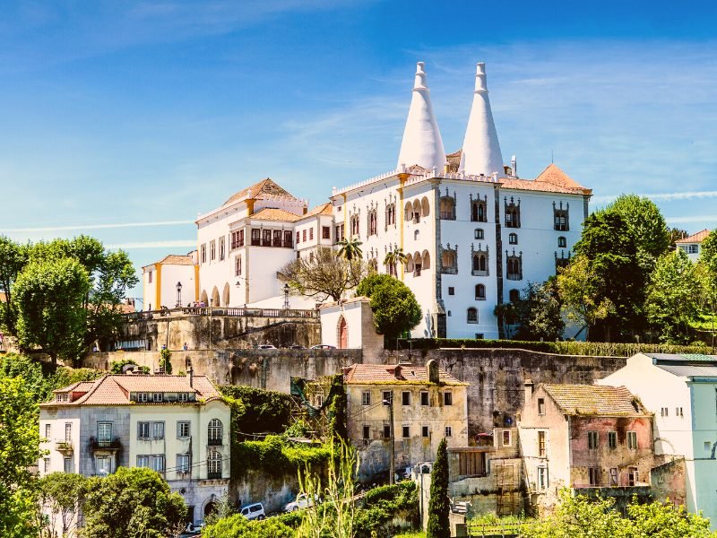 The historic Sintra Palace, white with two triangular spires, atop a hill in the middle of Sintra Town, on a sunny day visiting the city.