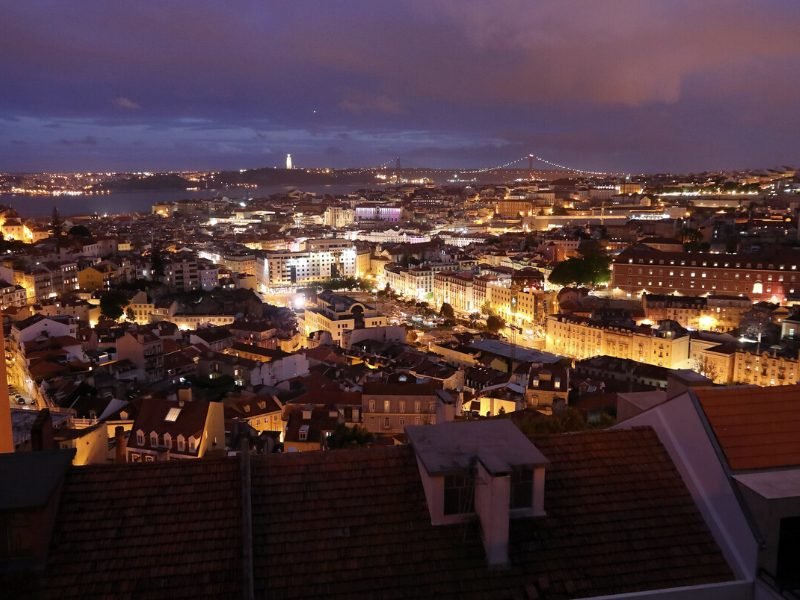 Night view of Lisbon city center with lit-up avenues and tagus river in the distance.