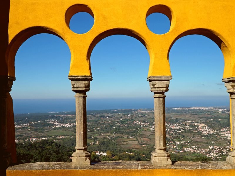 View of the coastline and the Atlantic ocean as seen from three yellow archways, part of the architecture of the famous Pena Palace