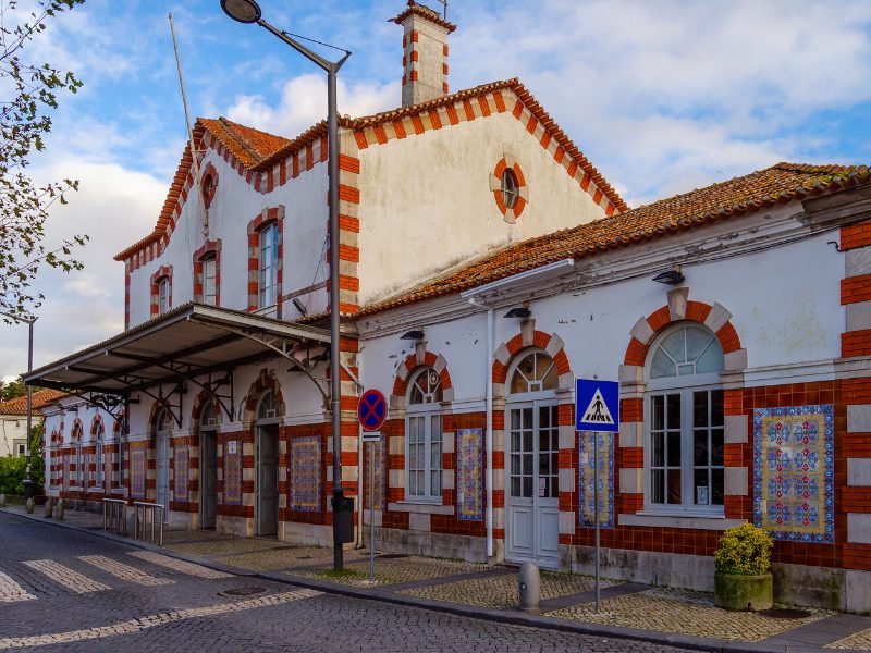 The white and red Sintra train station with azulejo-style mosaic paneling on the walls of the train station on a sunny, partly cloudy day.