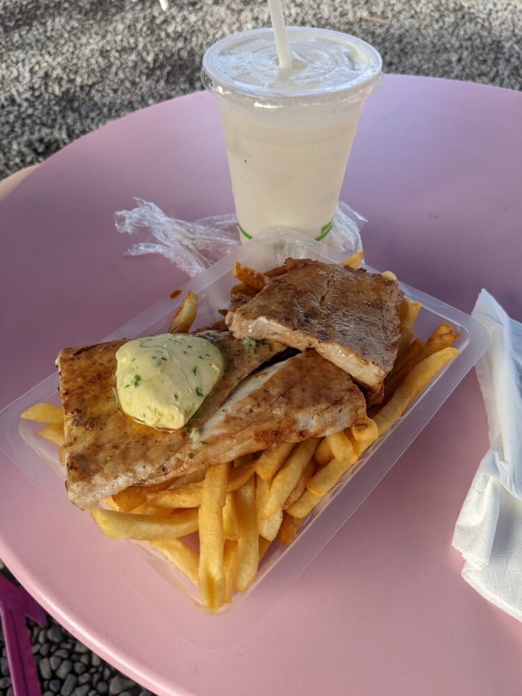 Grilled tuna fish with herb butter and BBQ sauce and fries served as a local eatery food truck on a beach in Tahiti Iti with a virgin pina colada.
