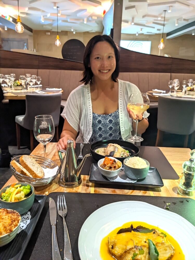 Allison's partner enjoying a fine dining meal in Papeete Tahiti consisting of fish, sides, while holding a glass of wine