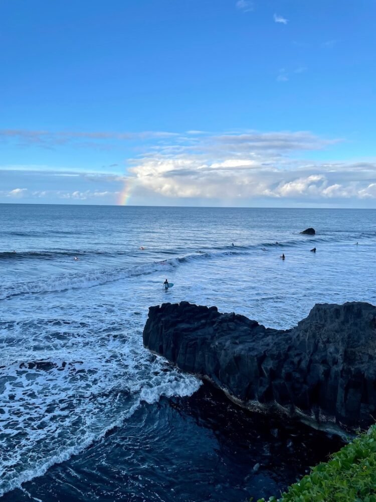 Rainbow on the horizon with surfers in the water on the east coast of tahiti in the late afternoon