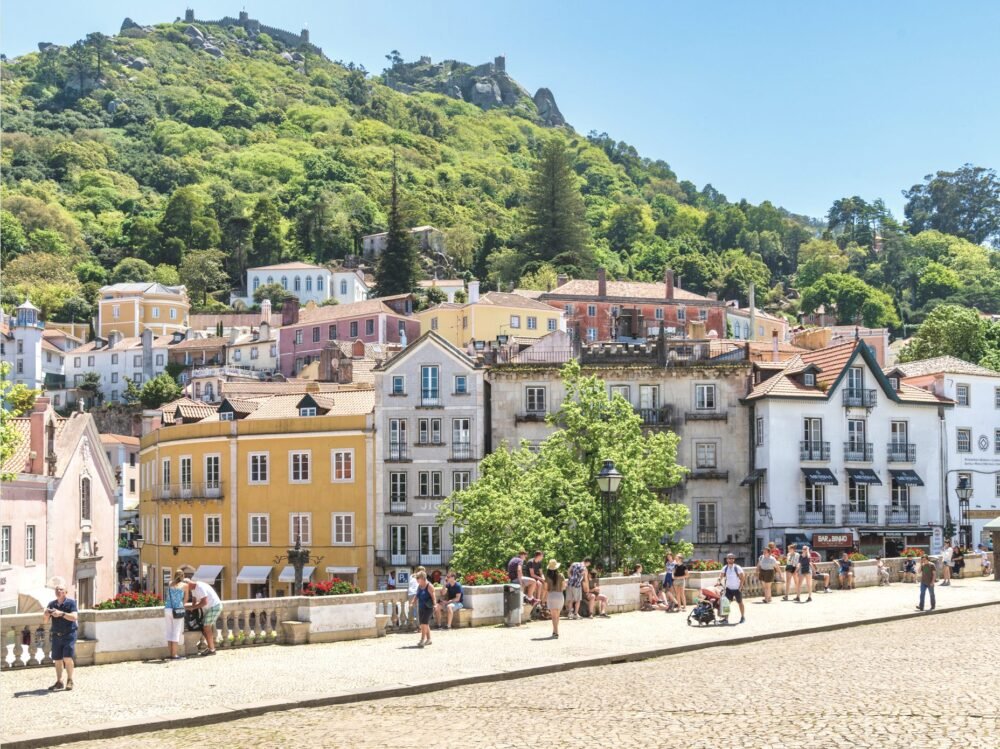 The downtown of Sintra in summer, with people walking around and enjoying the sights of downtown, a view of a castle visible high atp a hill