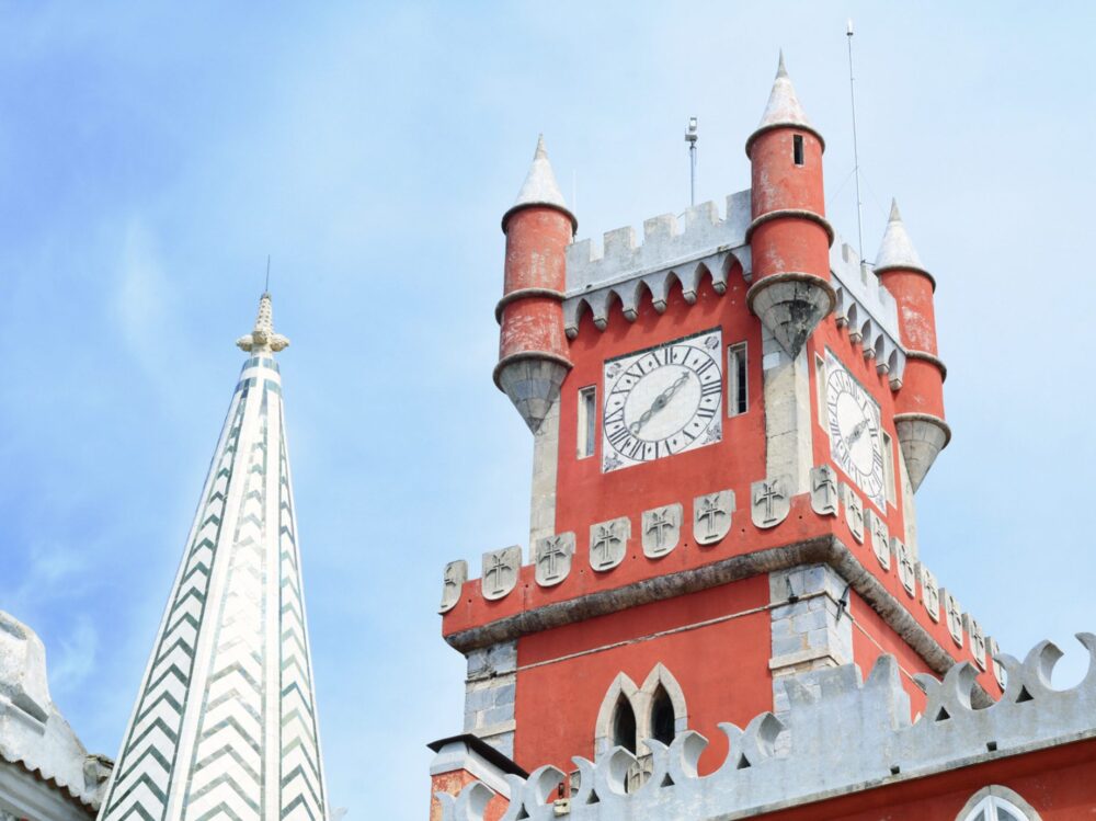 View of the iconic red clock tower in Pena Palace, with roman numeral clock face and four spires atop the clock tower
