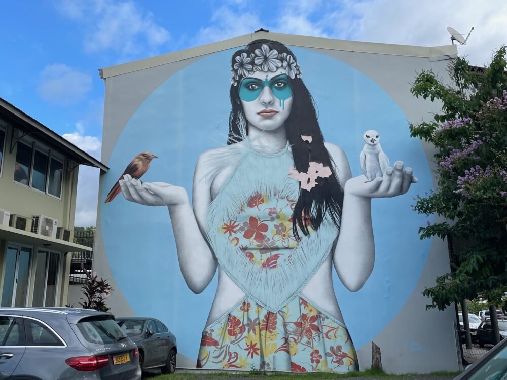 Street art in Papeete of a girl holding two birds in her hands with blue makeup and background