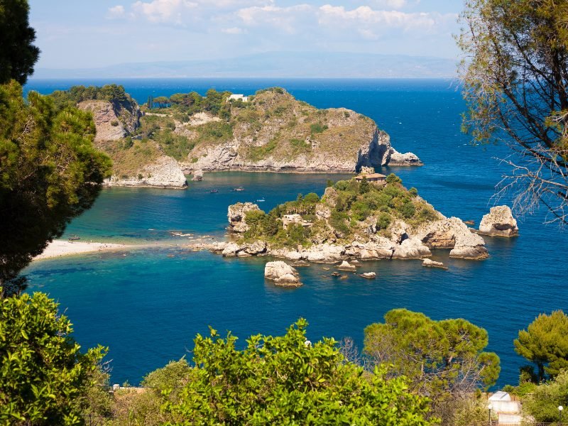 The view of the sandy spit leading to Isola Bella, a small islet off the coast of Taormina. People enjoying the beach, kayaking and sunbathing.