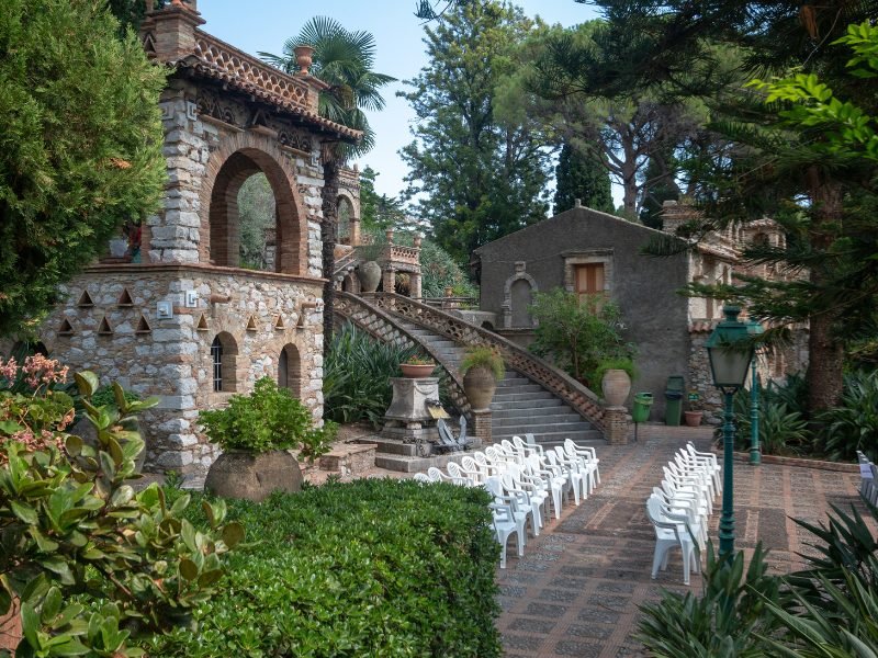 The famous Villa Comunale at a public park near the Greek Theater, stone buildings with pathways, bridges, trees, and chairs set out to enjoy a view.