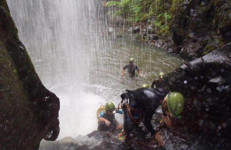 People doing a canyoning activity climbing up and down a waterfall with rappelling gear in Tahiti