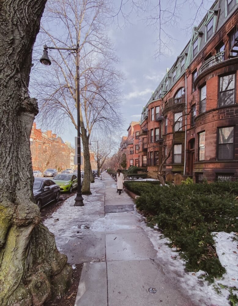 View of a snowy street in Boston, a woman walking down the street in the distance, and red brownstones typical of the city