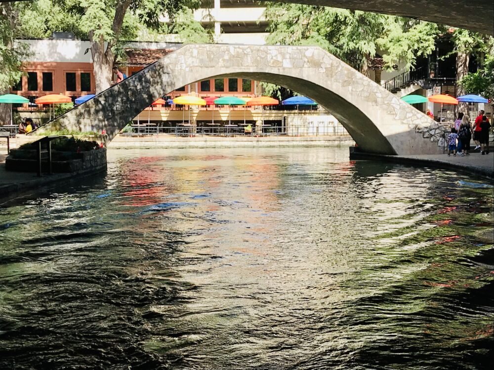 The view of the san antonio river walk with calm water and a bridge leading you over the river