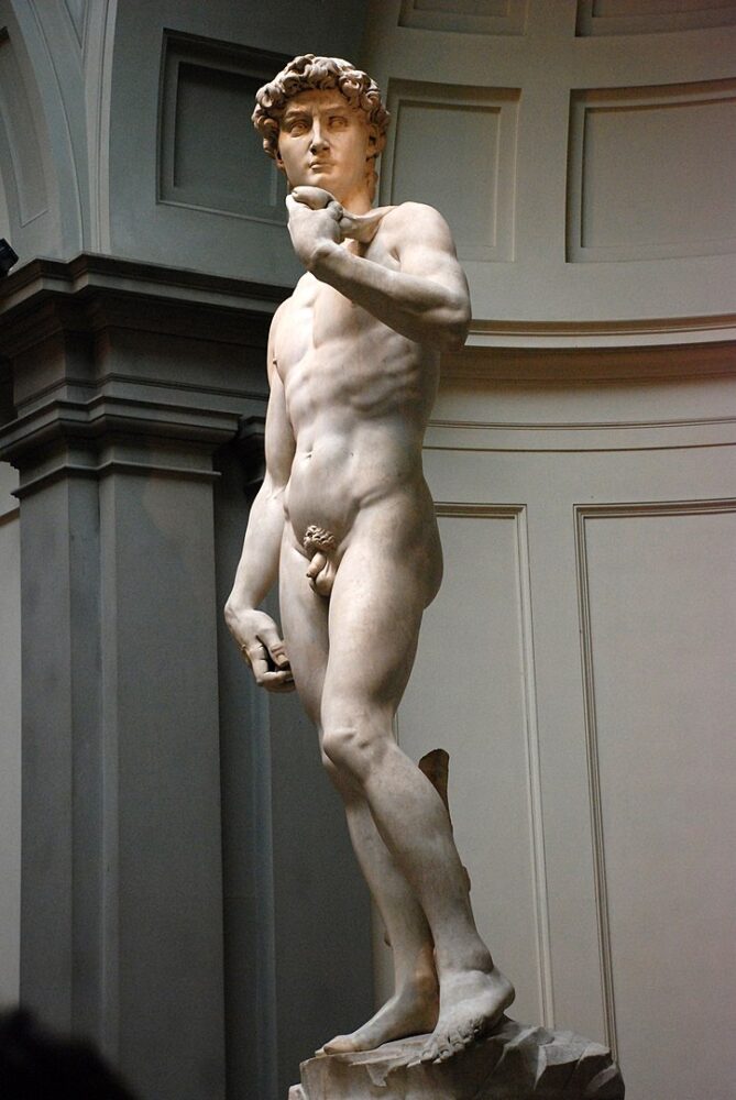 View of Michelangelo's David from the side, with soft light falling on the statue while inside a gallery