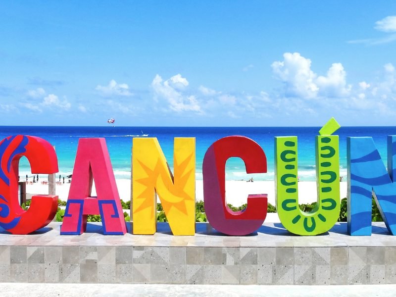 Rainbow Cancun sign in front of a beach called Delfines beach with white sand and brilliant blue waters