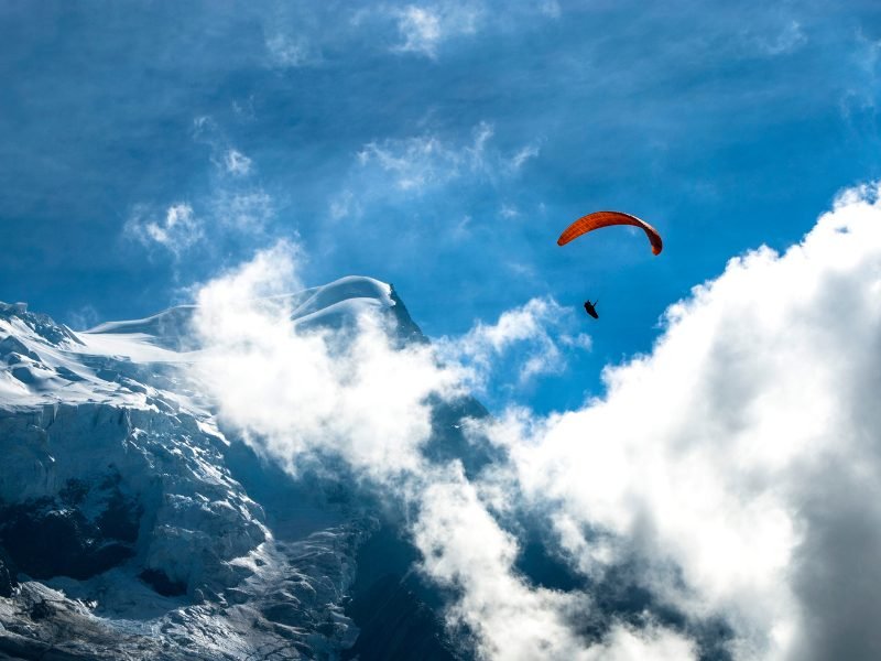 Person paragliding with a red paragliding umbrella over the peak of the Mont Blanc foothills