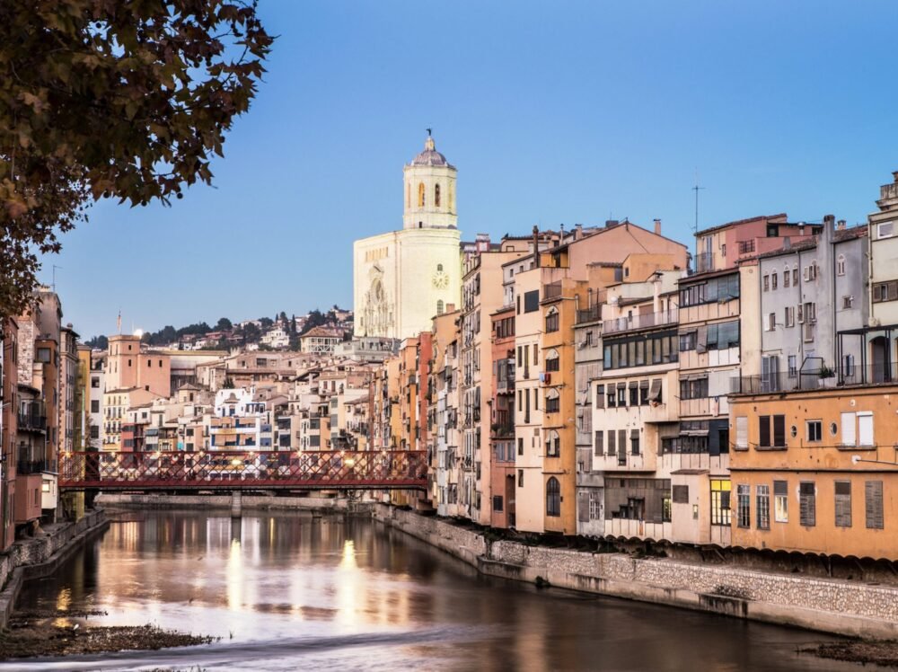 The river going down the middle of Girona, splitting it into the new town and the older town, with the cathedral on a hill in the distance, and the city's famous red bridge