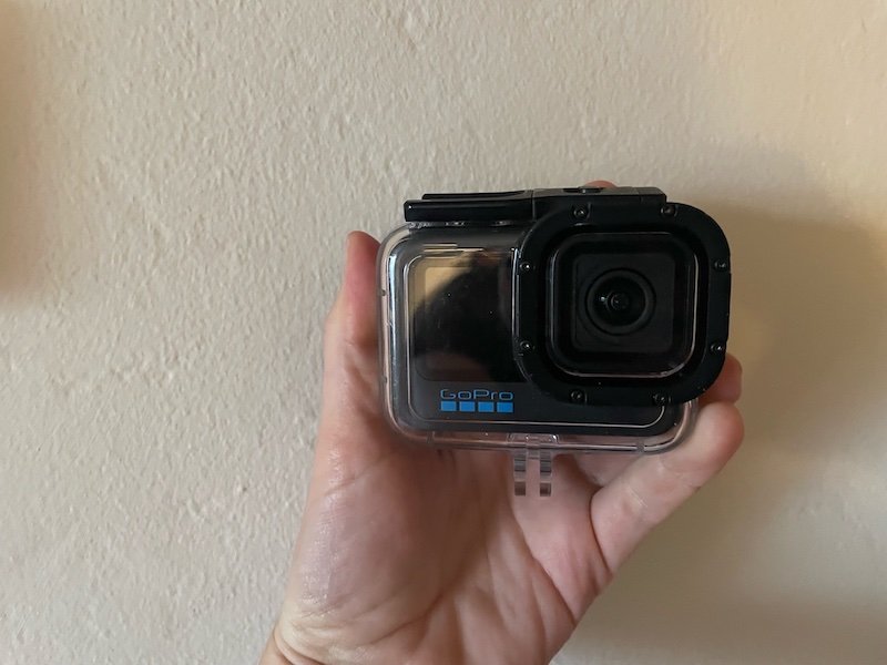 Allison holding her GoPro 11 in the protective GoPro housing made for diving, holding the camera up against a white wall