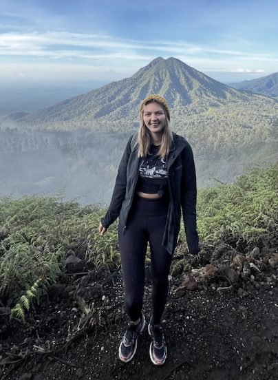 The author Megan Judd standing in front of a volcano wearing hiking clothes and sporty shoes