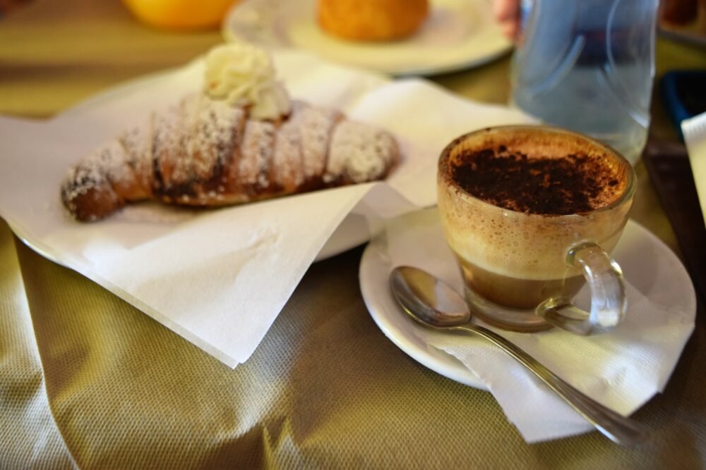 Cappuccino and pastry from Sicily with lots of powdered sugar on top of it and cream