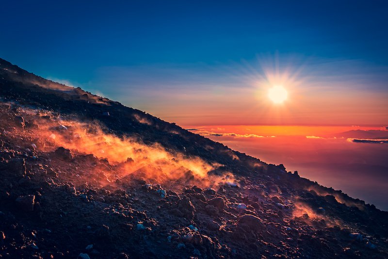 View of a sunset as seen from Mount etna, dramatic light show with the sun bouncing off the clouds, reflecting steam coming from the active volcano