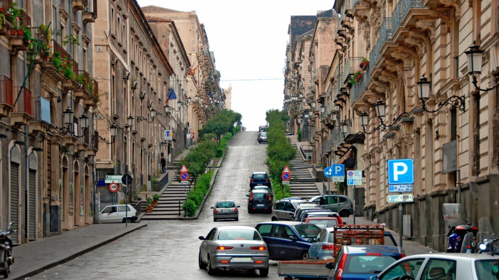 Steep paved town street at Catania with cars, Sicily, showing the difficulty of parking with many cars already parked in the limited parking spots available.