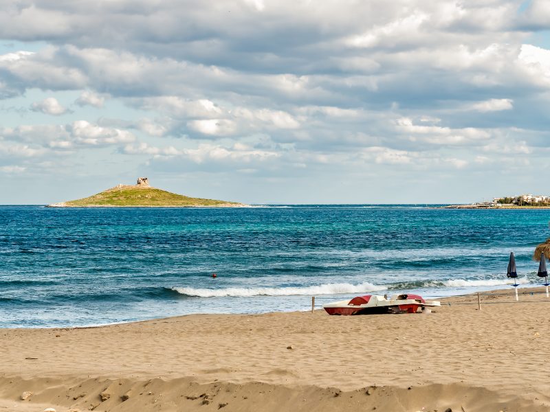 View of Isola delle Femmine from the beach, with a boat, umbrellas, and soft sand in front of the small island