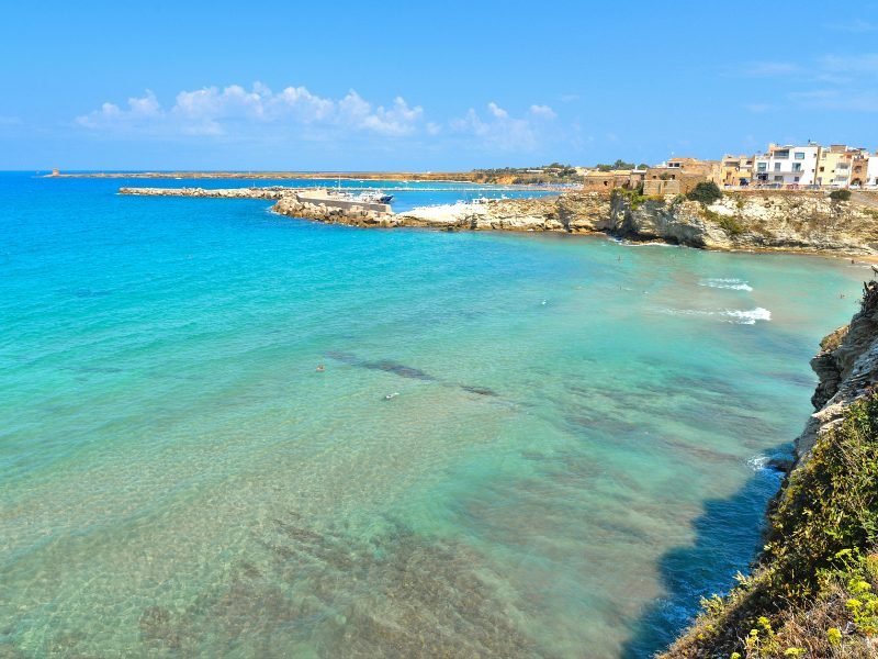 People swimming in the shallow waters and clear beautiful sea of La Praiola with houses on the cliffside behind them